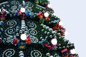 A fragment of a huge Christmas tree with many ornaments, gift boxes and luminous lamps. Photo of a decorated Christmas tree close-up with copy space