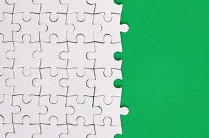 Fragment of a folded white jigsaw puzzle on the background of a green plastic surface. Texture photo with copy space for text