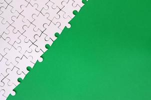 Fragment of a folded white jigsaw puzzle on the background of a green plastic surface. Texture photo with copy space for text