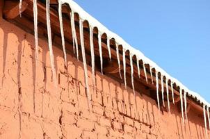 A lot of long icicles hang under the roof of a red brick building photo