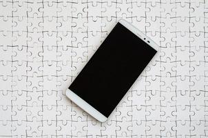 A modern big smartphone with a touch screen lies on a white jigsaw puzzle in an assembled state photo