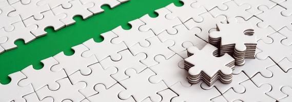 The green path is laid on the platform of a white folded jigsaw puzzle. The missing elements of the puzzle are stacked nearby. Texture image with space for text photo