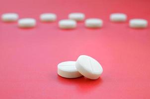 A few white tablets lie on a bright red background surface. Background image on medical and pharmaceutical topics photo