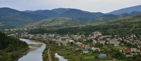 A beautiful view of the village of Mezhgorye, Carpathian region. A lot of residential buildings surrounded by high forest mountains and long river photo