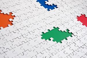 Close-up texture of a white jigsaw puzzle in assembled condition with missing elements, under which surfaces of different colors photo