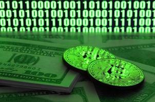 Two bitcoins lies on a pile of dollar bills on the background of a monitor depicting a binary code of bright green zeros and one units on a black background. Low key lighting photo