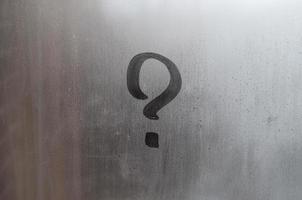 The inscription on glass, question mark concept. Question sign is painted on the surface of misted and wet window photo