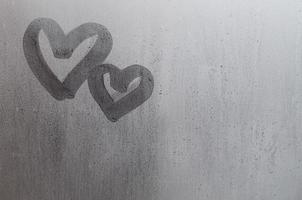 Couple of abstract blurred love heart symbol drawn by hand on the wet window glass with sunlight background. Template for Valentine Day postcards photo