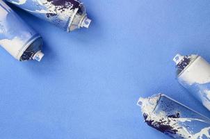 algunas latas de aerosol azul usadas con gotas de pintura se encuentran sobre una manta de tela suave y peluda de color azul claro. color de diseño femenino clásico. concepto de vandalismo de graffiti foto