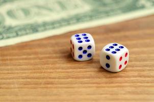 White dice are next to a dollar bill of US dollars on a wooden background. The concept of gambling with rates in monetary units photo