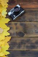 The old camera among a set of yellowing fallen autumn leaves on a background surface of natural wooden boards of dark brown color photo