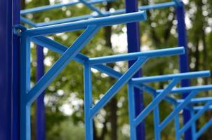 tubos de metal azul y barras transversales contra un campo de deportes callejeros para entrenar en atletismo. equipo de gimnasia atlética al aire libre. foto macro con enfoque selectivo y fondo extremadamente borroso