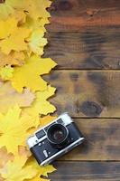 The old camera among a set of yellowing fallen autumn leaves on a background surface of natural wooden boards of dark brown color photo