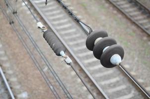 Electrical insulators on the contact wires on the background of a blurred railway track. Macro photo with selective focus