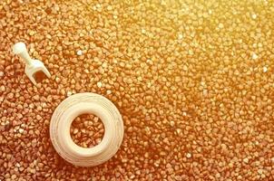 Background image of a large pile of buckwheat, in the middle of which lies a small jug and a wooden spatula for cereals photo