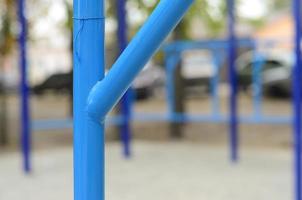 Blue metal pipes and cross-bars against a street sports field for training in athletics. Outdoor athletic gym equipment. Macro photo with selective focus and extremely blurred background