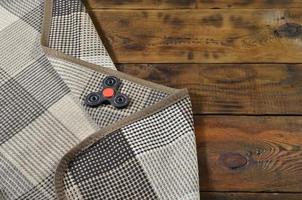 A rare wooden handmade spinner lies on a checkered plaid on a brown wooden background surface. Trendy stress relieving toy photo