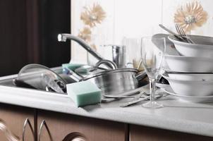 A huge pile of unwashed dishes in the kitchen sink and on the countertop photo