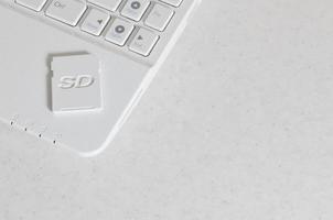 A compact SD memory card lies on a white netbook. The digital information storage device is ready for use. Concept of modern technologies photo