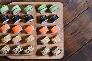 Sushi set of a number of rolls is located on a wooden cutting board on a table in the kitchen of a sushi bar. A traditional dish of oriental cuisine photo