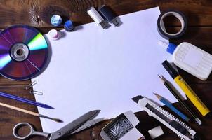 A school or office still life with a white blank sheet of paper and many office supplies. The school supplies lie on a brown wooden background. Place for text photo