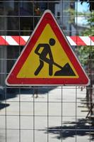 The warning sign under construction is attached to a metal mesh fence with a red and white striped signal tape photo