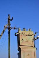 Old and obsolete electrical transformer against the background of a cloudless blue sky. Device for distribution of supply of high-voltage energy photo