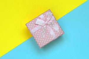 Small pink gift box lie on texture background of fashion pastel blue and yellow colors paper in minimal concept photo
