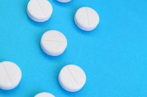 A few white tablets lie on a bright blue background surface. Background image on medical and pharmaceutical topics photo