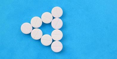 Several white tablets lie on a bright blue background in the form of an even triangle. Background image on medicine and pharmaceutical topics photo