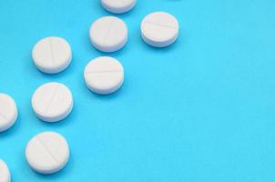 A few white tablets lie on a bright blue background surface. Background image on medical and pharmaceutical topics photo