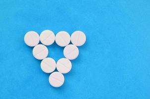 Several white tablets lie on a bright blue background in the form of an even triangle. Background image on medicine and pharmaceutical topics photo