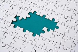 Close-up texture of a white jigsaw puzzle in assembled state with missing elements forming a blue pad for text. Copy space photo