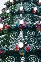 A fragment of a huge Christmas tree with many ornaments, gift boxes and luminous lamps. Photo of a decorated Christmas tree close-up