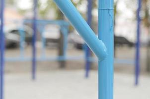 Blue metal pipes and cross-bars against a street sports field for training in athletics. Outdoor athletic gym equipment. Macro photo with selective focus and extremely blurred background