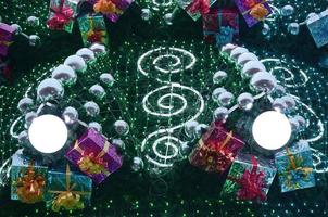 A fragment of a huge Christmas tree with many ornaments, gift boxes and luminous lamps. Photo of a decorated Christmas tree close-up