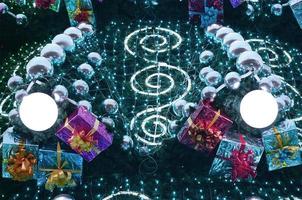 A fragment of a huge Christmas tree with many ornaments, gift boxes and luminous lamps. Photo of a decorated Christmas tree close-up