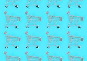 Shopping addiction, shopping lover or shopaholic concept. Many small empty shopping carts perform a pattern on a pastel colored paper background. Flat lay composition, top view photo