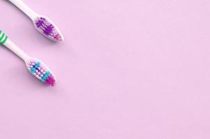 Two toothbrushes lie on a pastel pink background photo
