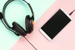 Black headphones and smartphone lies on a colorful pastel pink background photo