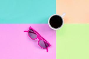 Small white coffee cup and pink sunglasses on background of fashion pastel pink, blue, coral and lime colors photo