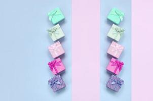 Small gift boxes of different colors with ribbons lies on a violet and pink background photo