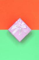 Small pink gift box lie on texture background of fashion pastel turquoise and red colors paper photo