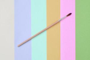 un nuevo pincel se encuentra en el fondo de textura de papel de color rosa pastel, azul, verde, amarillo, violeta y beige de moda foto