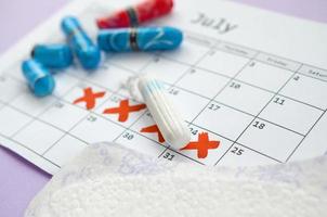 Menstrual pads and tampons on menstruation period calendar with red cross marks lies on lilac background photo