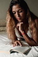 Latina woman concentrating and enjoying a book lying on her bed. photo