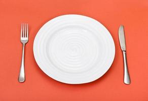 above view of white plate, fork, knife on red photo