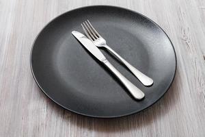 black plate with parallel knife, spoon on gray photo