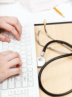 physician works on white PC keyboard photo