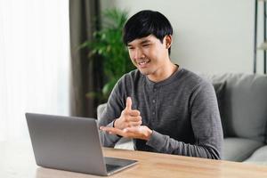 Young Asian man deaf disabled using laptop computer for online video conference call learning and communicating in sign language. photo